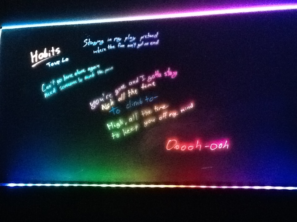 A clear sheet of acrylic sits on top of an LED strip. The room is dark. Light passes through the  acrylic, then escapes wherever marker dye is present. The lyrics of Tove Lo's “Habits” are written on the board, glowing in an array of different colors.
