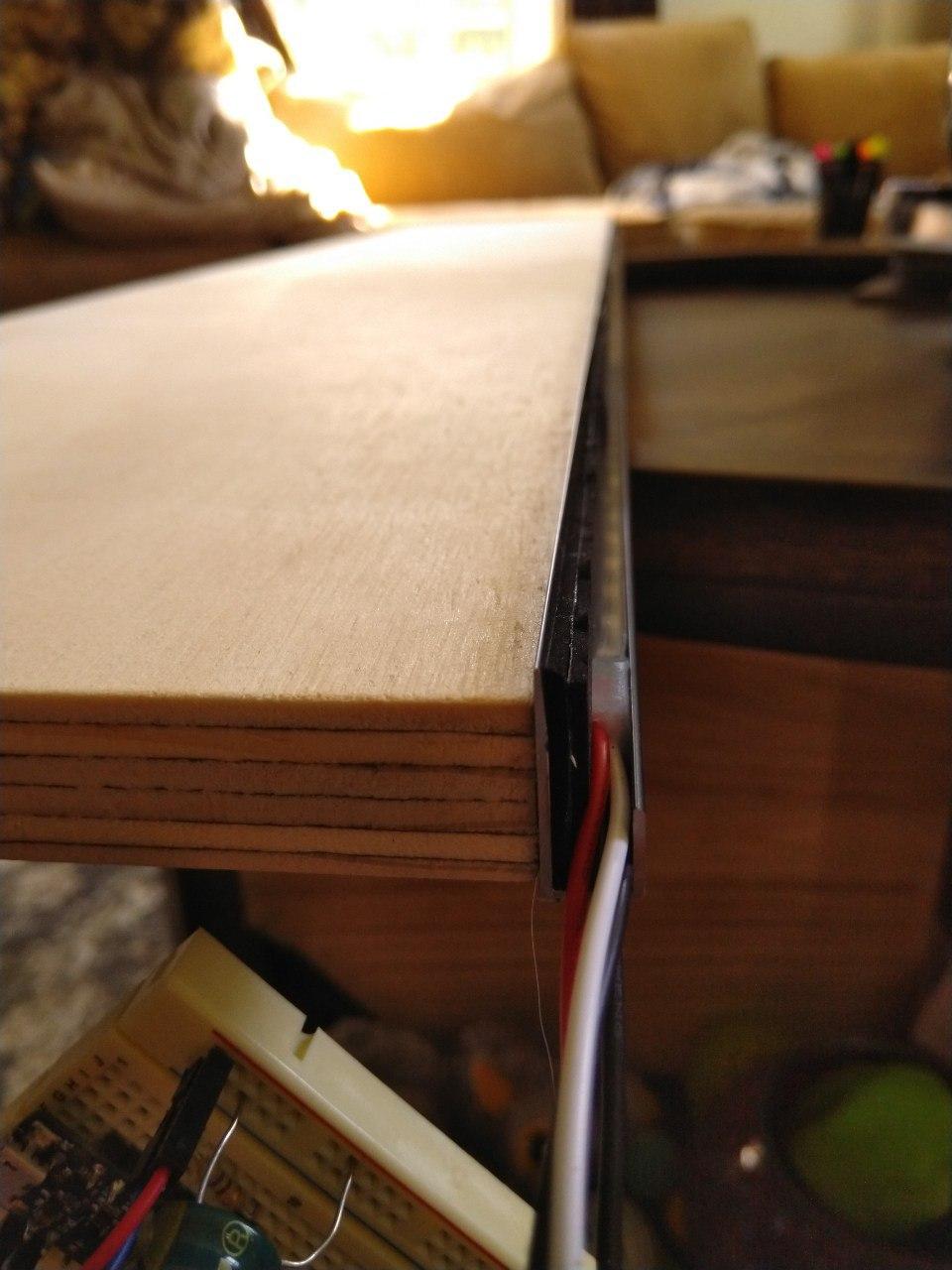 An aluminum J-channel mounted on the inside of a plywood shelf. An LED strip is fitted inside.